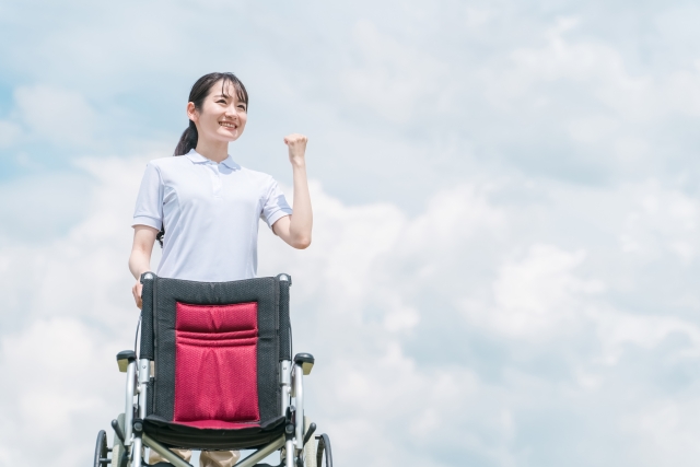 青空の下、車いすを押して外出に付き添うスタッフ